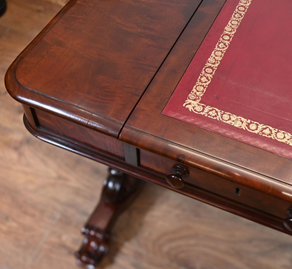 A late Victorian mahogany writing table featuring a central red leather skiver with gold tooling, two frieze drawers, turned end supports, and a curved stretcher. View VII