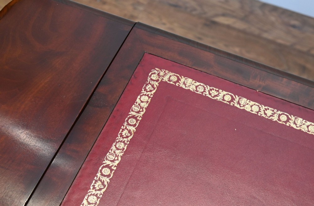 A late Victorian mahogany writing table featuring a central red leather skiver with gold tooling, two frieze drawers, turned end supports, and a curved stretcher. View VIII