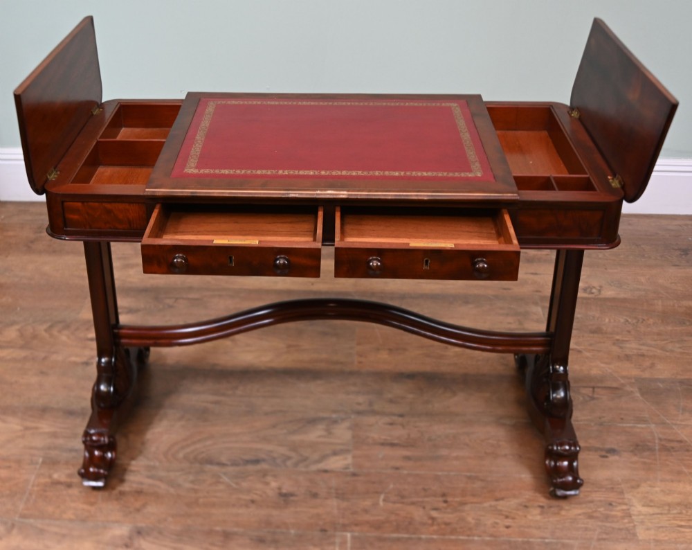 A late Victorian mahogany writing table featuring a central red leather skiver with gold tooling, two frieze drawers, turned end supports, and a curved stretcher. View IX