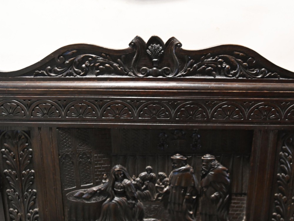 A late 19th-century dark carved walnut hall bench featuring a pictorial relief back panel, scrolled armrests, and turned stretchers. View V