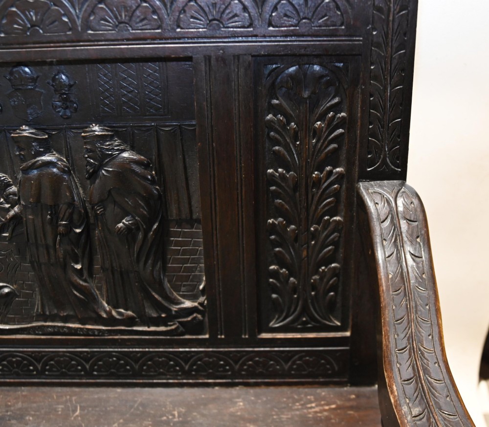A late 19th-century dark carved walnut hall bench featuring a pictorial relief back panel, scrolled armrests, and turned stretchers. View VI