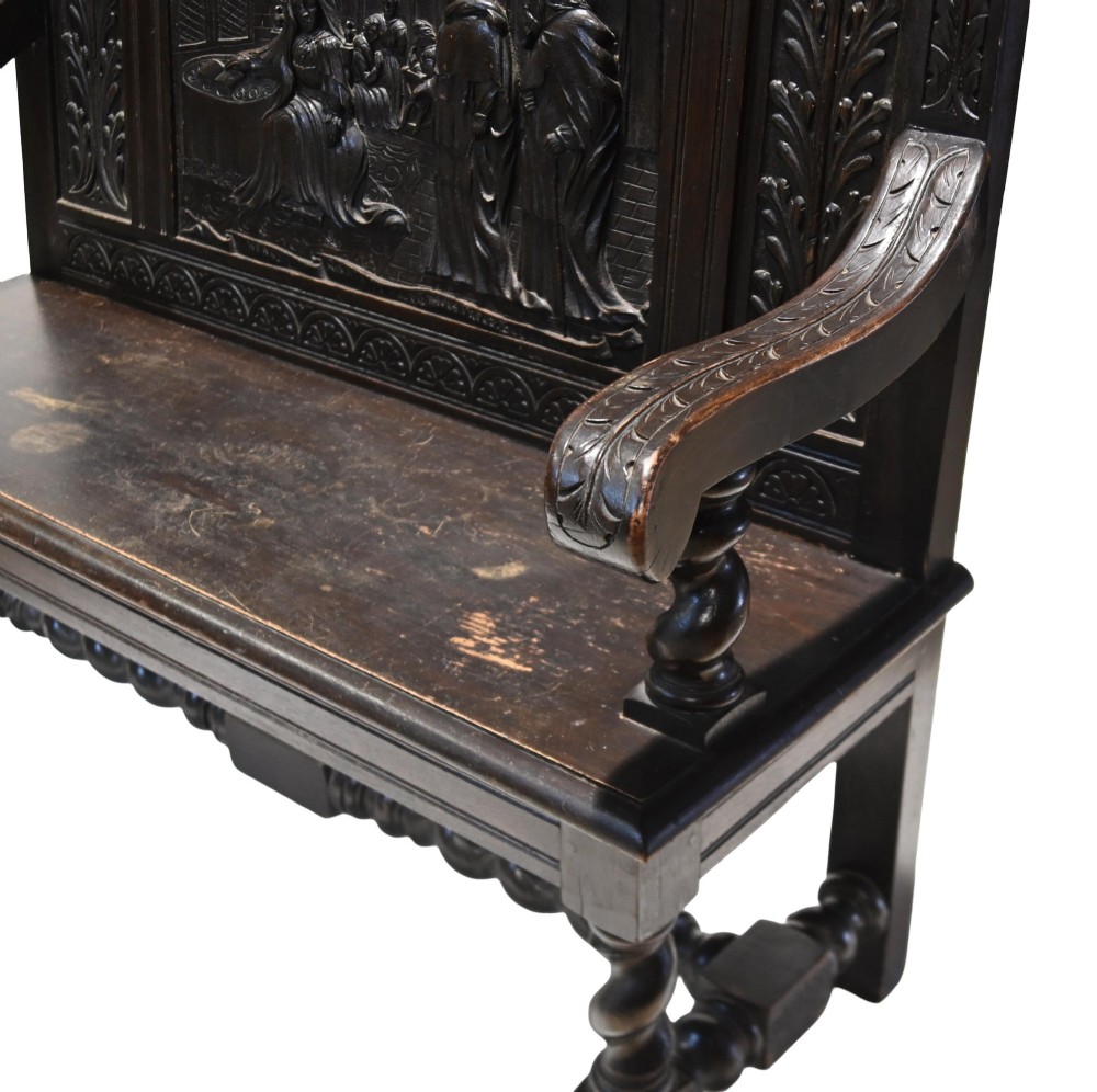 A late 19th-century dark carved walnut hall bench featuring a pictorial relief back panel, scrolled armrests, and turned stretchers. View X