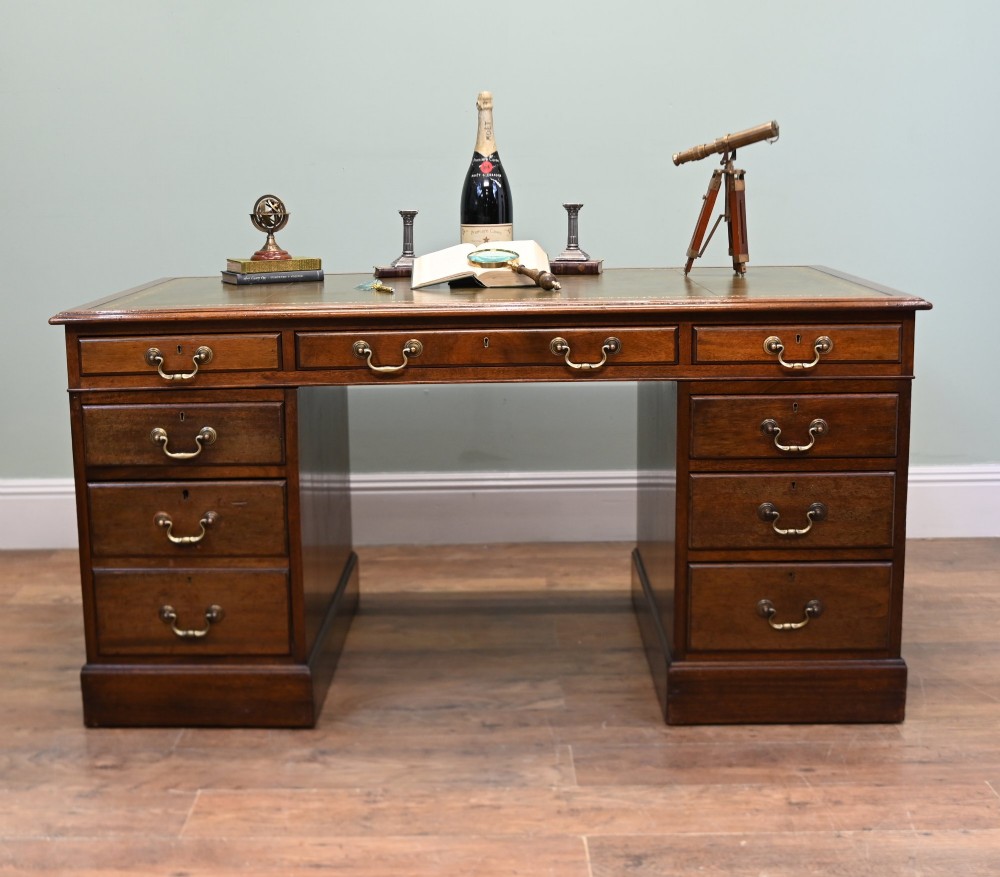 A Victorian mahogany pedestal desk featuring nine brass-handled drawers and a green leather gilt-tooled writing surface resting on a solid plinth base. View III