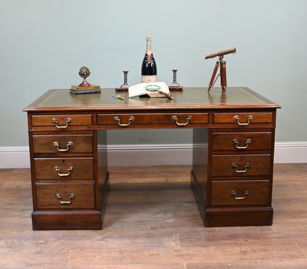 A Victorian mahogany pedestal desk featuring nine brass-handled drawers and a green leather gilt-tooled writing surface resting on a solid plinth base. View IV