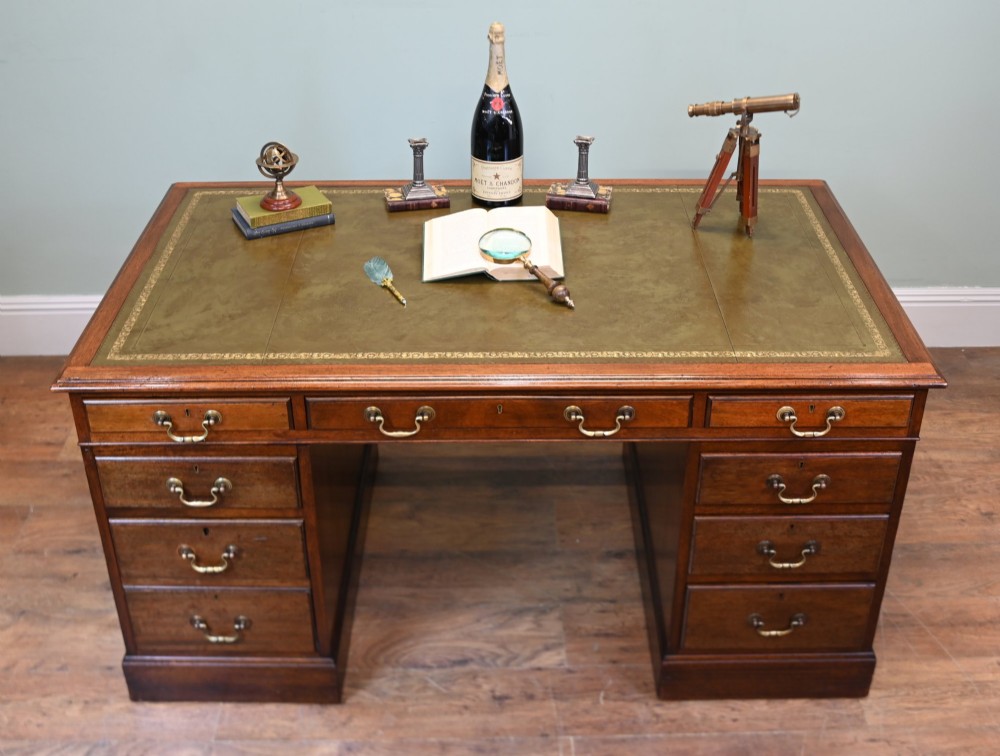 A Victorian mahogany pedestal desk featuring nine brass-handled drawers and a green leather gilt-tooled writing surface resting on a solid plinth base. View V