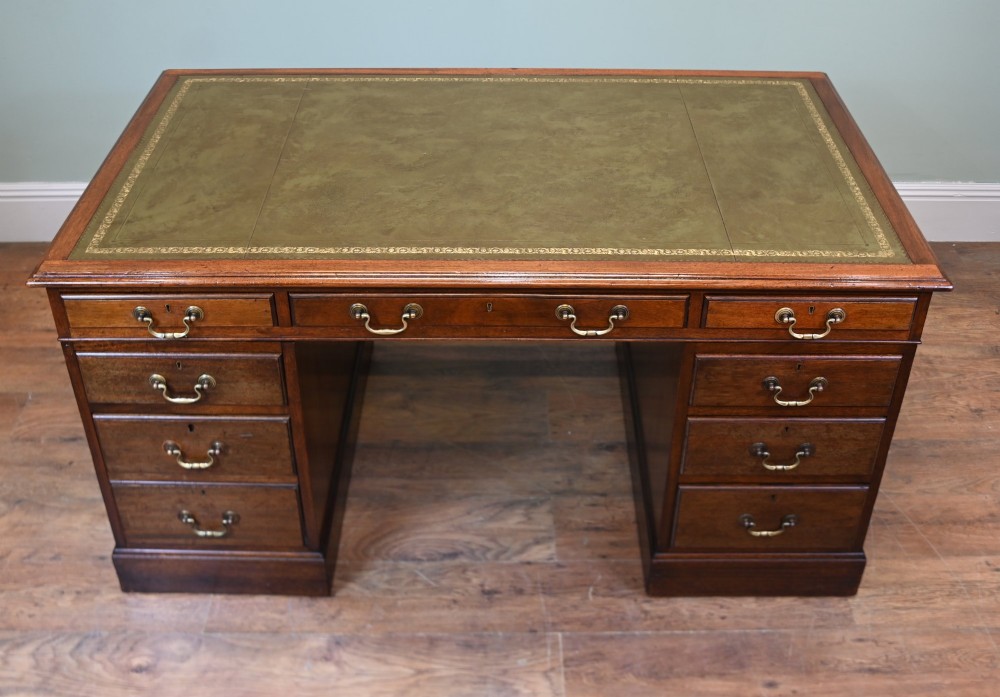 A Victorian mahogany pedestal desk featuring nine brass-handled drawers and a green leather gilt-tooled writing surface resting on a solid plinth base. View VI