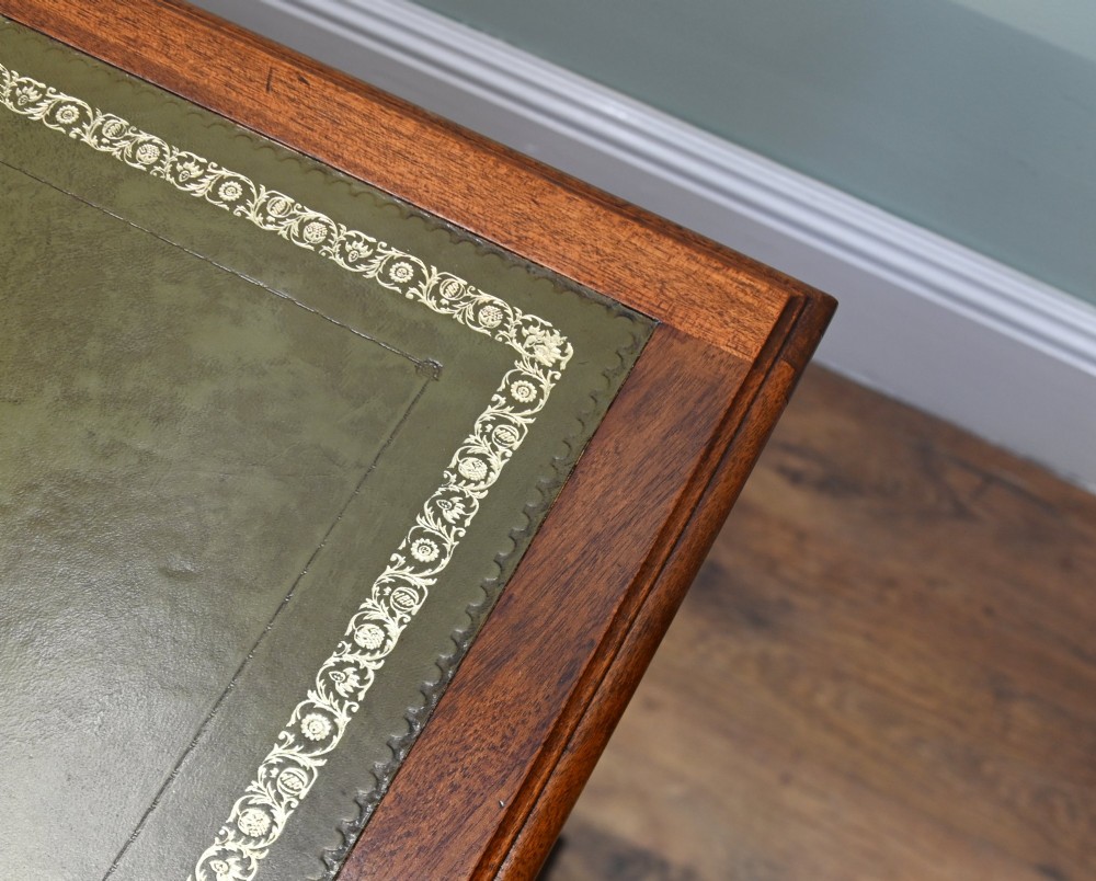 A Victorian mahogany pedestal desk featuring nine brass-handled drawers and a green leather gilt-tooled writing surface resting on a solid plinth base. View VII