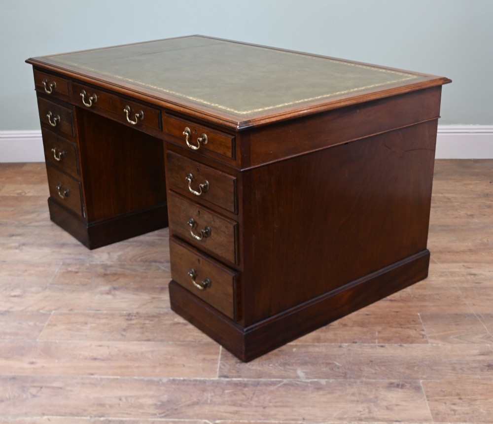 A Victorian mahogany pedestal desk featuring nine brass-handled drawers and a green leather gilt-tooled writing surface resting on a solid plinth base. View VIII
