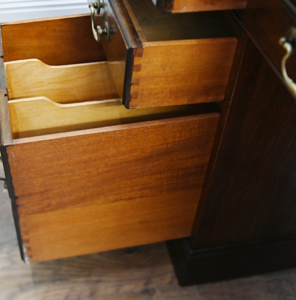A Victorian mahogany pedestal desk featuring nine brass-handled drawers and a green leather gilt-tooled writing surface resting on a solid plinth base. View XI