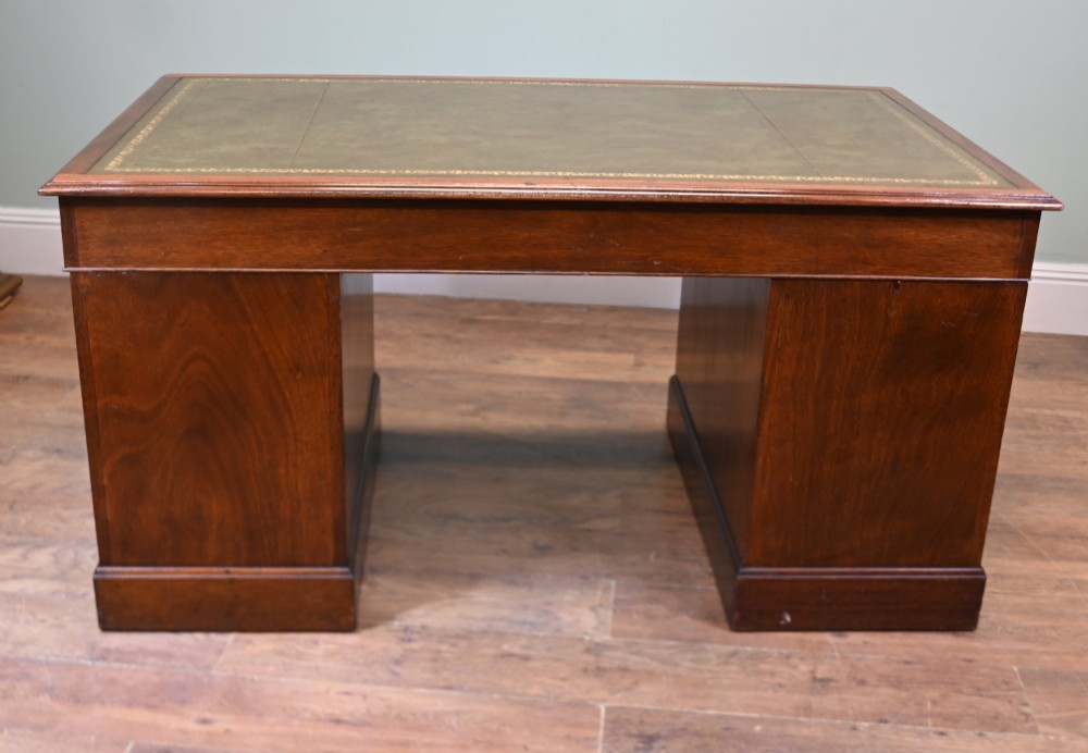 A Victorian mahogany pedestal desk featuring nine brass-handled drawers and a green leather gilt-tooled writing surface resting on a solid plinth base. View XII