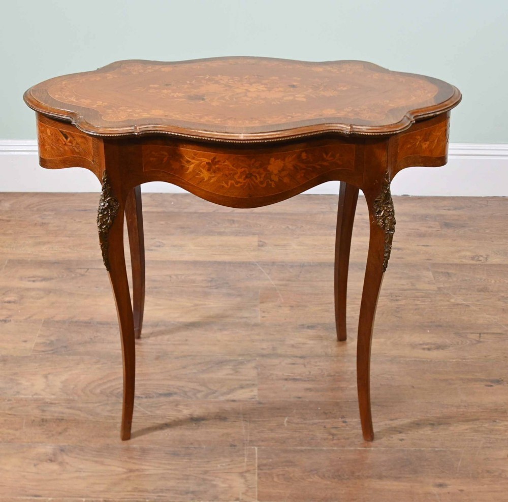A shaped French Louis XV style writing table crafted from warm brown wood featuring intricate floral marquetry inlay, cabriole legs, and bronze mounts.