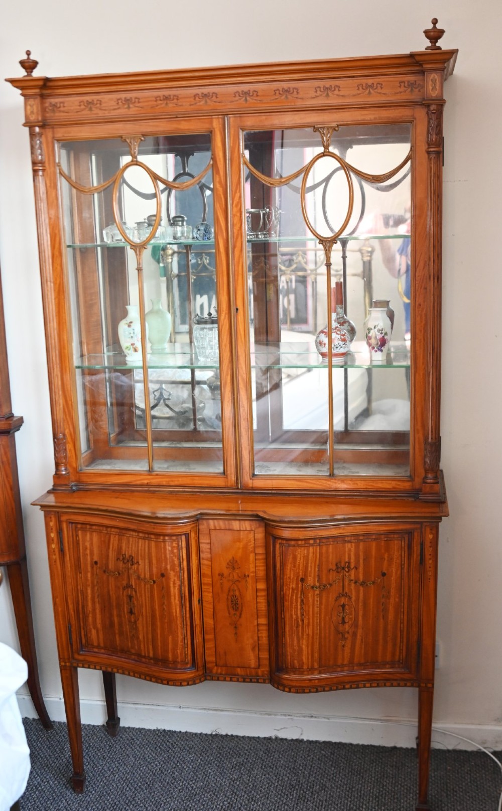 An Edwardian Sheraton Revival display cabinet in painted satinwood with glazed double doors, decorative oval glazing bars, and lower cupboard doors on slender square legs.