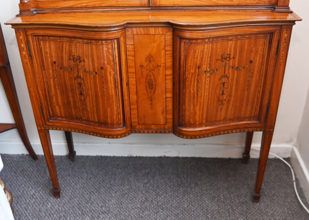 An Edwardian Sheraton Revival display cabinet in painted satinwood with glazed double doors, decorative oval glazing bars, and lower cupboard doors on slender square legs. View IV