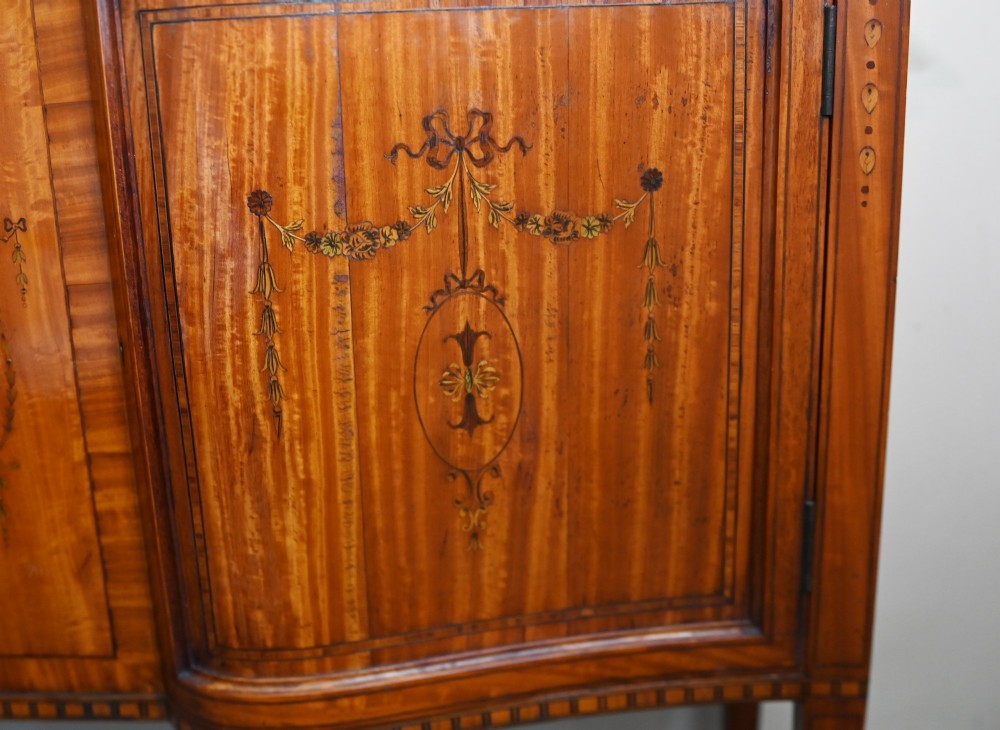 An Edwardian Sheraton Revival display cabinet in painted satinwood with glazed double doors, decorative oval glazing bars, and lower cupboard doors on slender square legs. View V