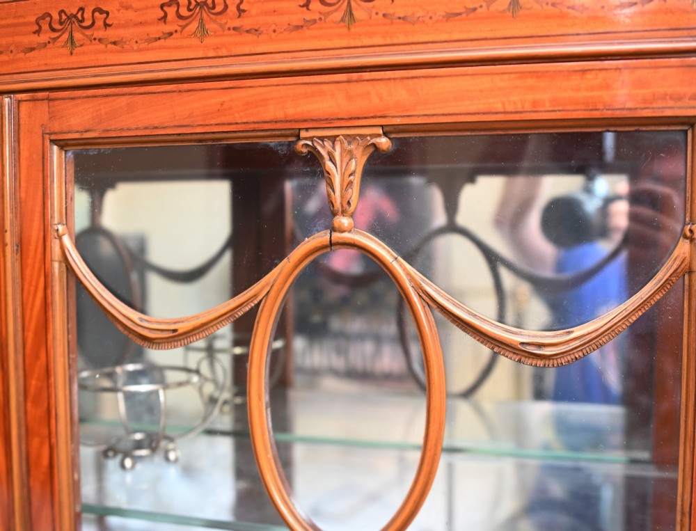An Edwardian Sheraton Revival display cabinet in painted satinwood with glazed double doors, decorative oval glazing bars, and lower cupboard doors on slender square legs. View XIII