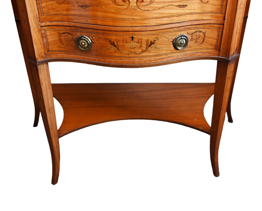 An Edwardian satinwood glazed display cabinet featuring classical urn marquetry, a swan-neck pediment, bowed glass sides, and drawers over tapered legs. View III