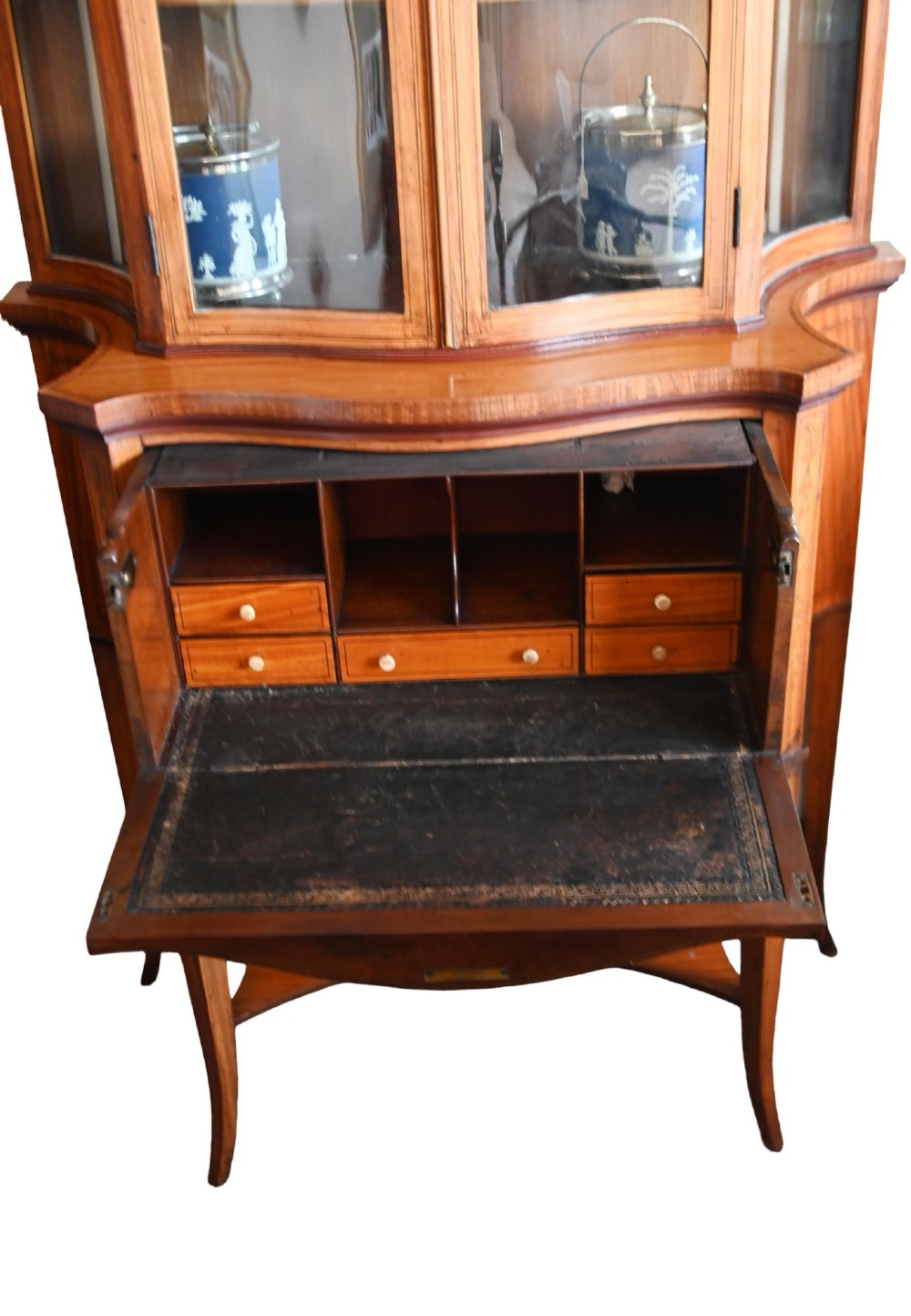 An Edwardian satinwood glazed display cabinet featuring classical urn marquetry, a swan-neck pediment, bowed glass sides, and drawers over tapered legs. View V