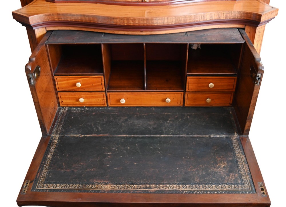 An Edwardian satinwood glazed display cabinet featuring classical urn marquetry, a swan-neck pediment, bowed glass sides, and drawers over tapered legs. View VI