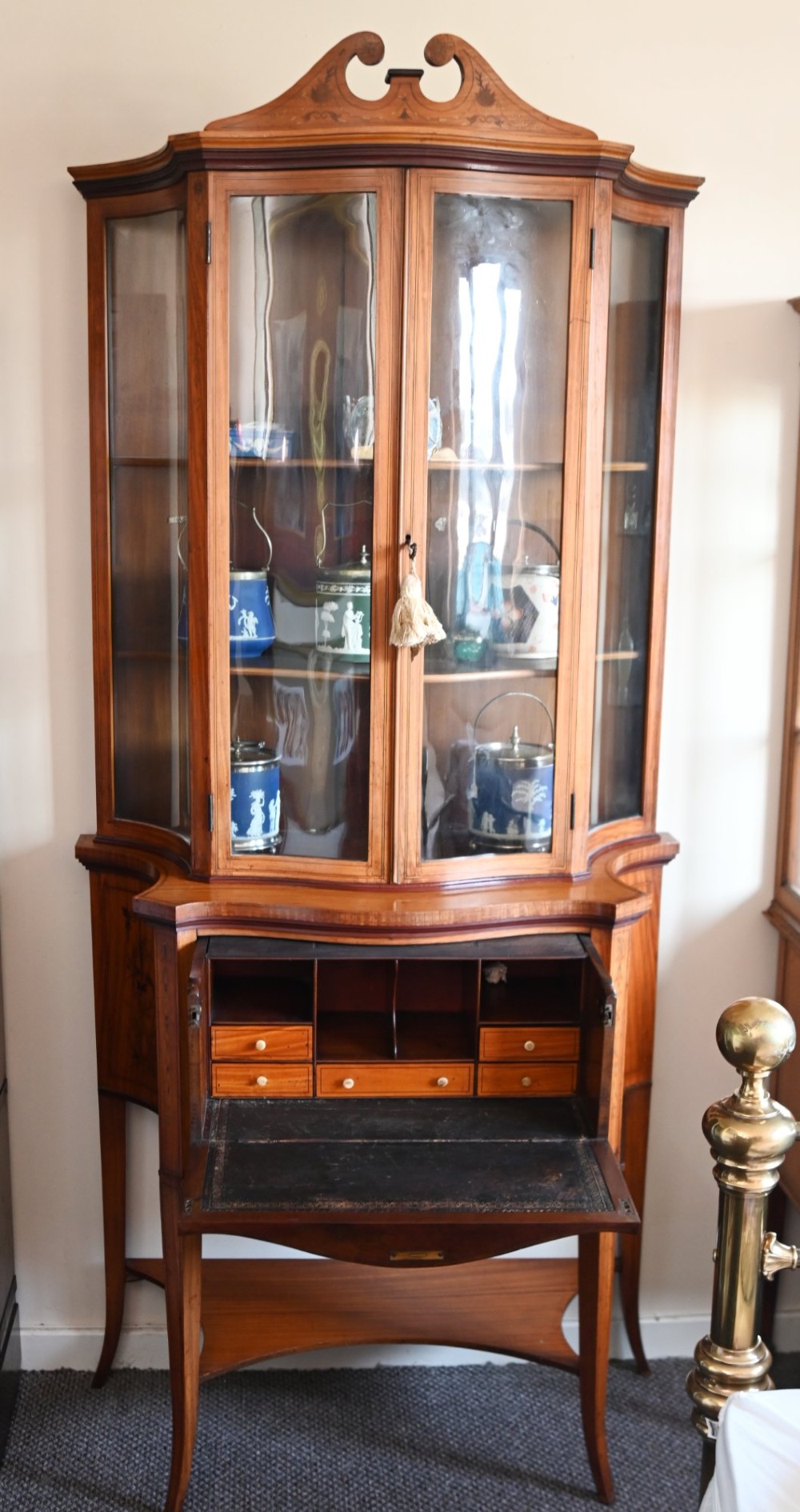 An Edwardian satinwood glazed display cabinet featuring classical urn marquetry, a swan-neck pediment, bowed glass sides, and drawers over tapered legs. View VII