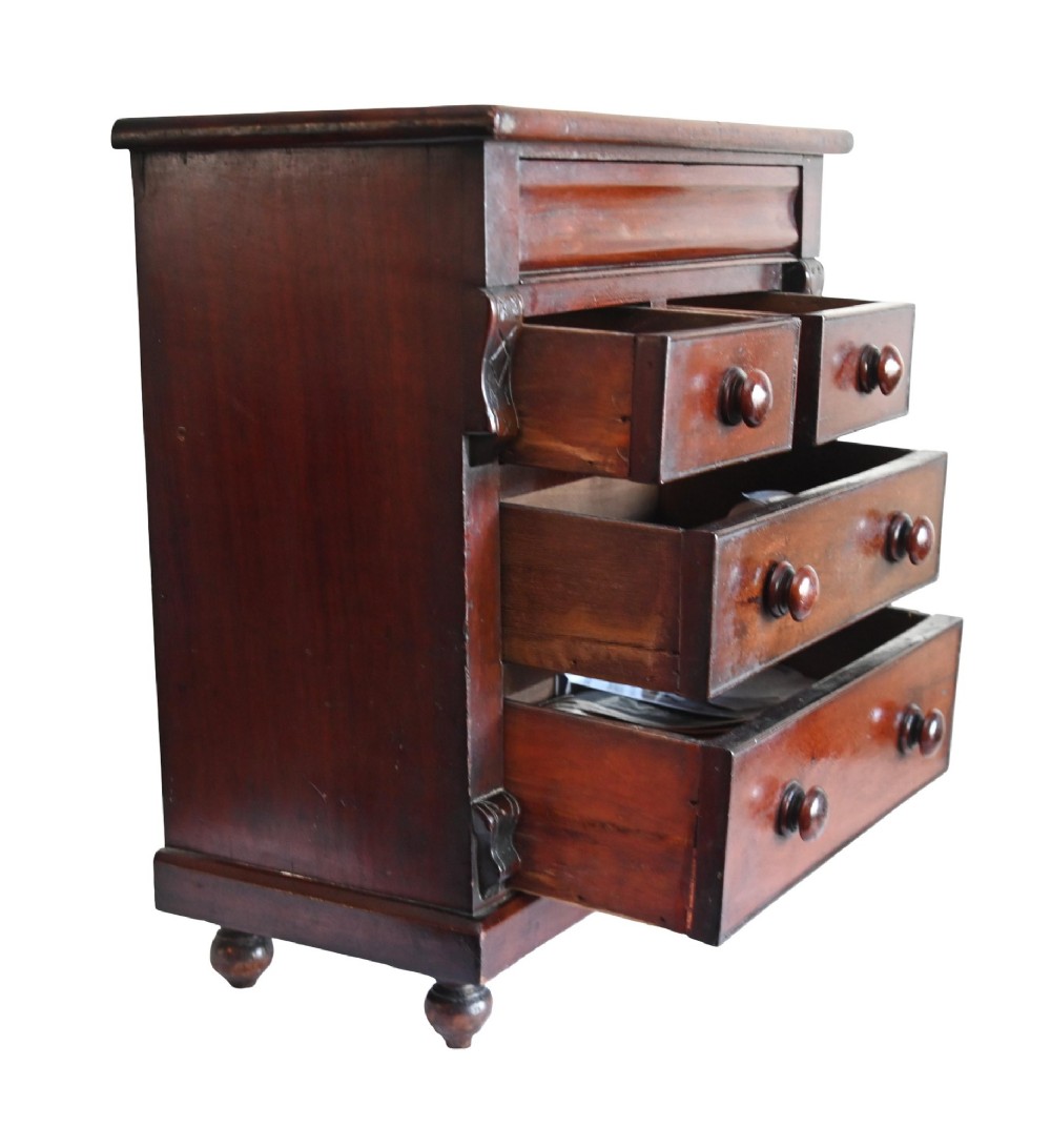 A 19th-century Scottish mahogany miniature apprentice chest featuring two short over two long drawers, a top cushion drawer, turned knobs, carved corbels, and turned feet. View V