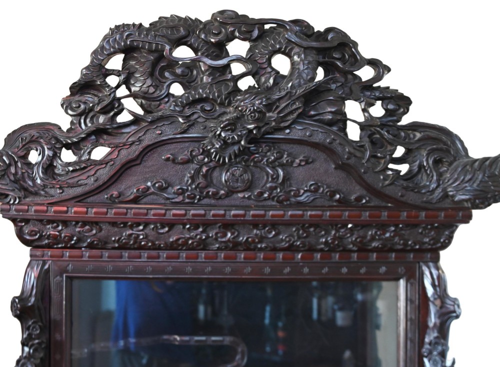 An intricately carved dark hardwood Japanese Meiji display cabinet featuring a dragon pediment, glazed door, and tiered asymmetrical shelves. View II
