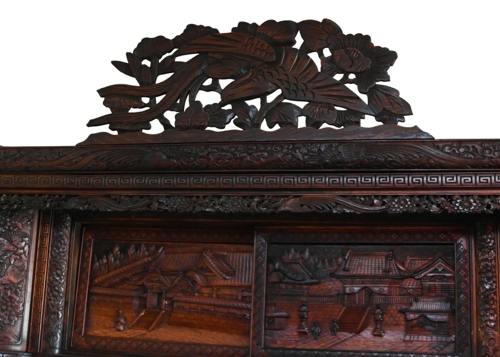 An intricately carved dark brown Japanese Meiji period display cabinet featuring asymmetrical open shelves, relief-carved cupboard doors, and a decorative cresting piece. View III