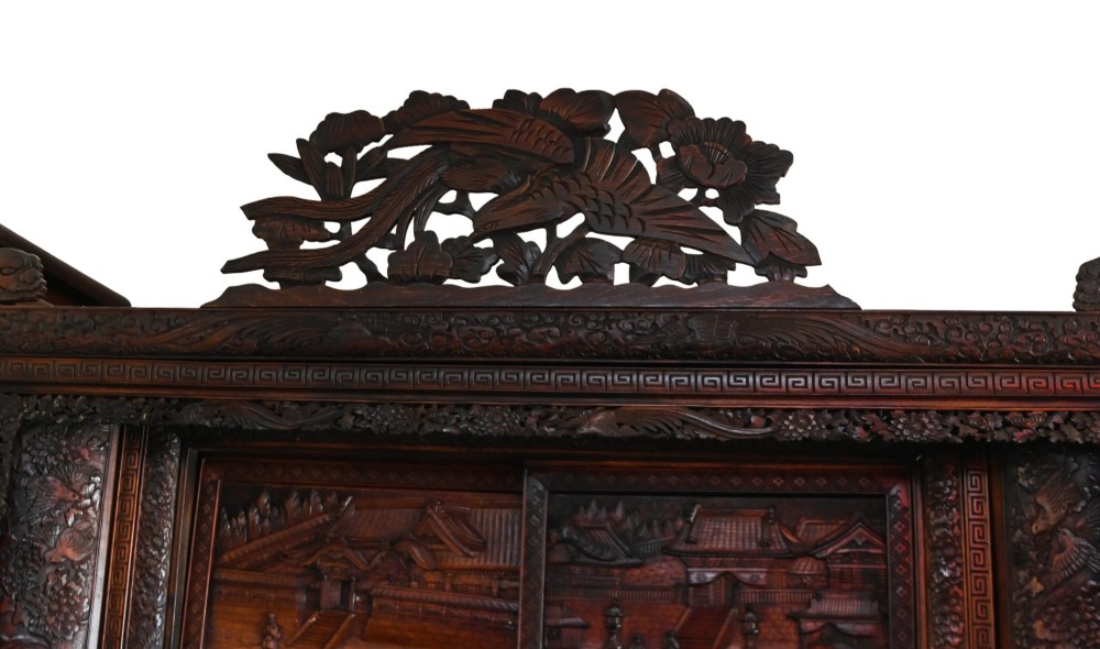 An intricately carved dark brown Japanese Meiji period display cabinet featuring asymmetrical open shelves, relief-carved cupboard doors, and a decorative cresting piece. View IV