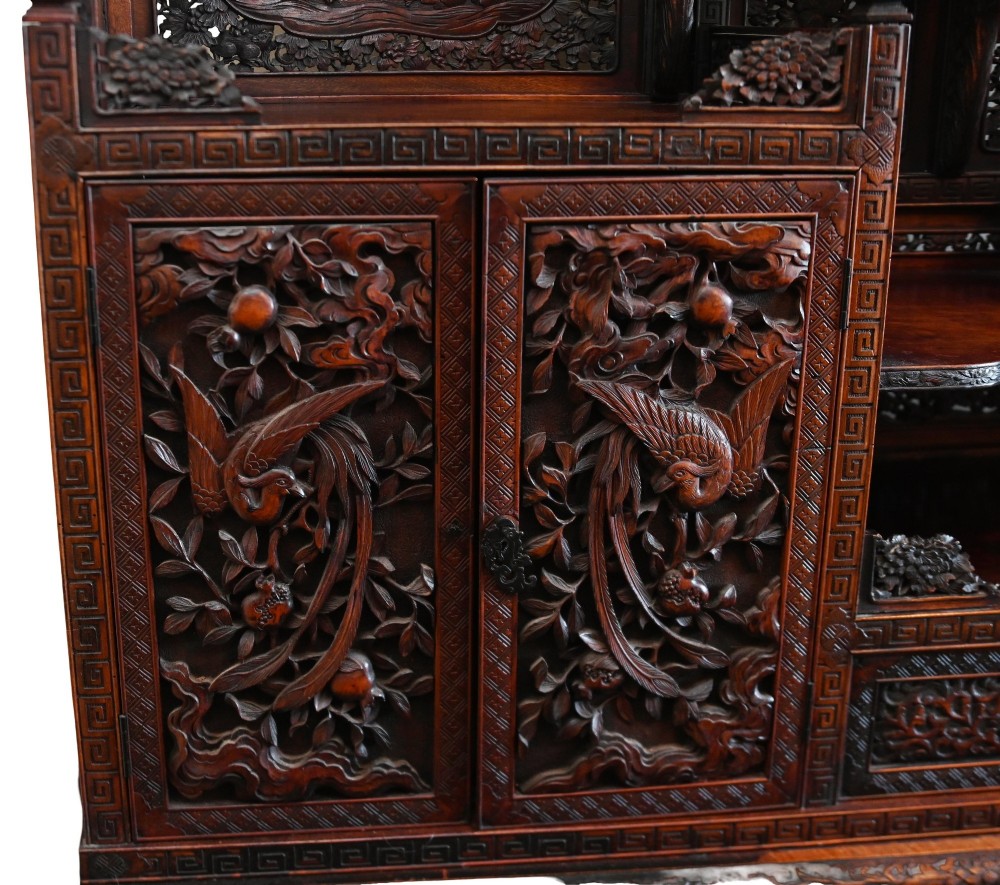 An intricately carved dark brown Japanese Meiji period display cabinet featuring asymmetrical open shelves, relief-carved cupboard doors, and a decorative cresting piece. View VII