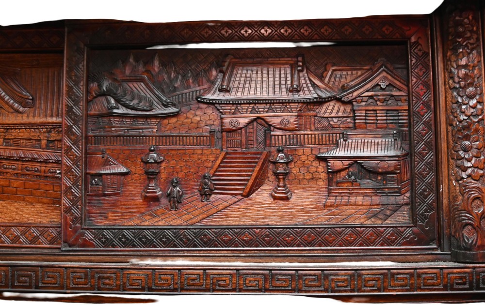 An intricately carved dark brown Japanese Meiji period display cabinet featuring asymmetrical open shelves, relief-carved cupboard doors, and a decorative cresting piece. View VIII