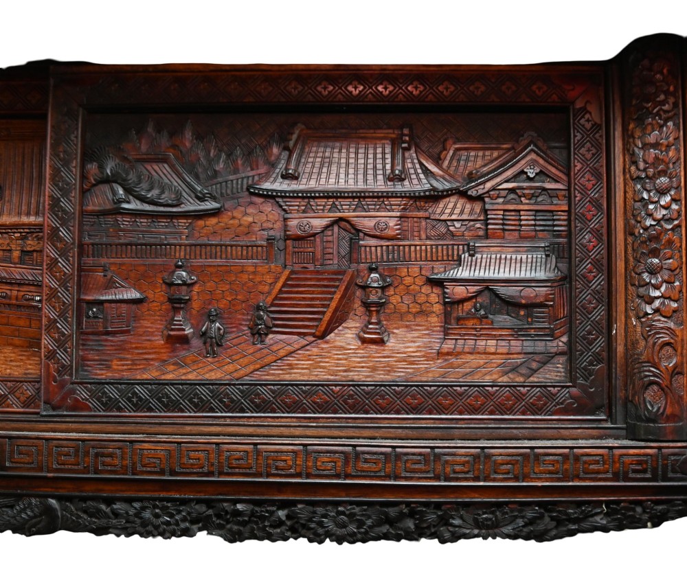 An intricately carved dark brown Japanese Meiji period display cabinet featuring asymmetrical open shelves, relief-carved cupboard doors, and a decorative cresting piece. View X