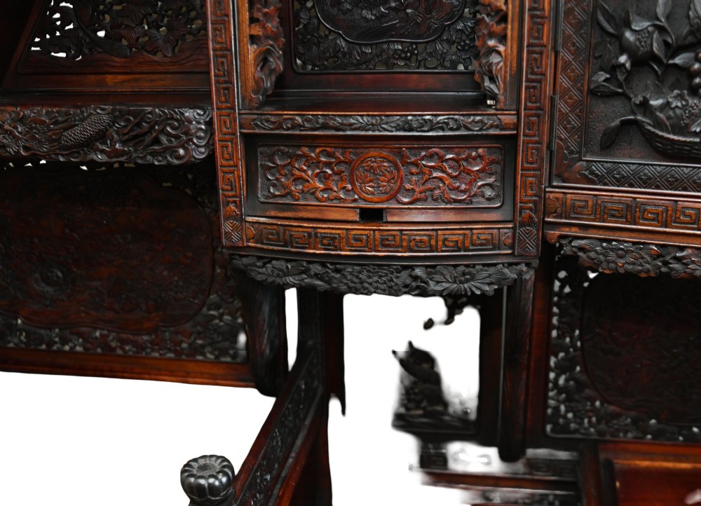 An intricately carved dark brown Japanese Meiji period display cabinet featuring asymmetrical open shelves, relief-carved cupboard doors, and a decorative cresting piece. View XII