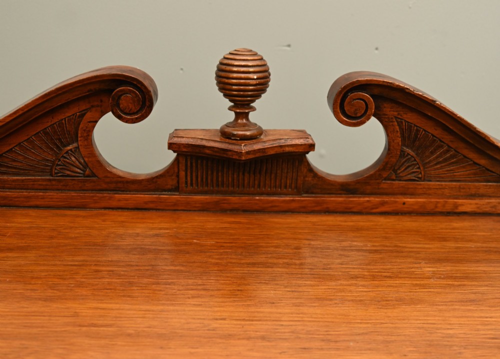 A William IV mahogany chiffonier side cabinet featuring a scroll-carved back gallery, central turned finial, carved rosette accents, and twin flame mahogany cupboard doors. View III