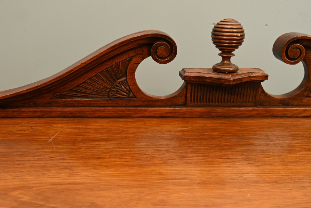 A William IV mahogany chiffonier side cabinet featuring a scroll-carved back gallery, central turned finial, carved rosette accents, and twin flame mahogany cupboard doors. View IV