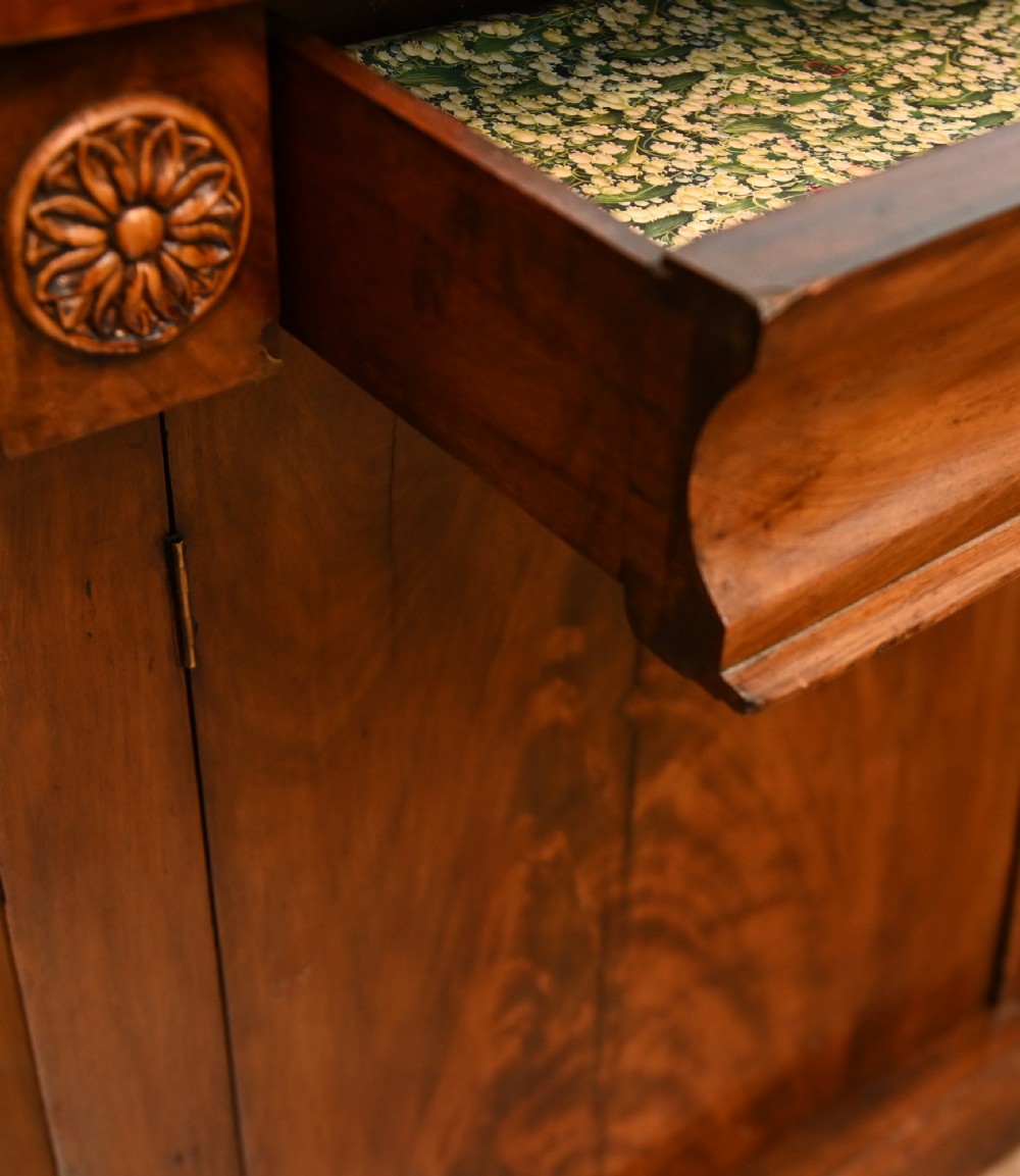 A William IV mahogany chiffonier side cabinet featuring a scroll-carved back gallery, central turned finial, carved rosette accents, and twin flame mahogany cupboard doors. View VIII
