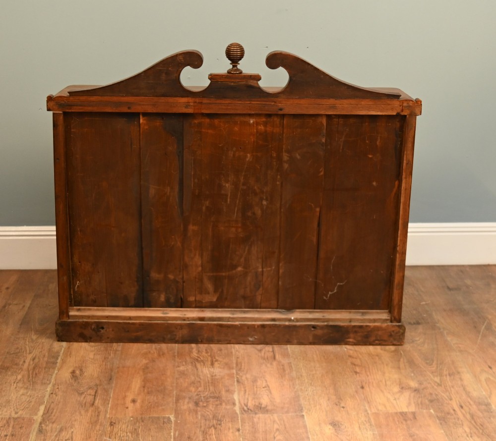 A William IV mahogany chiffonier side cabinet featuring a scroll-carved back gallery, central turned finial, carved rosette accents, and twin flame mahogany cupboard doors. View X