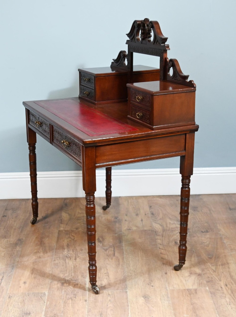 A mahogany ladies writing desk featuring a red leather inset writing surface, a central mirror superstructure flanked by drawers, and turned legs on castors. View VII