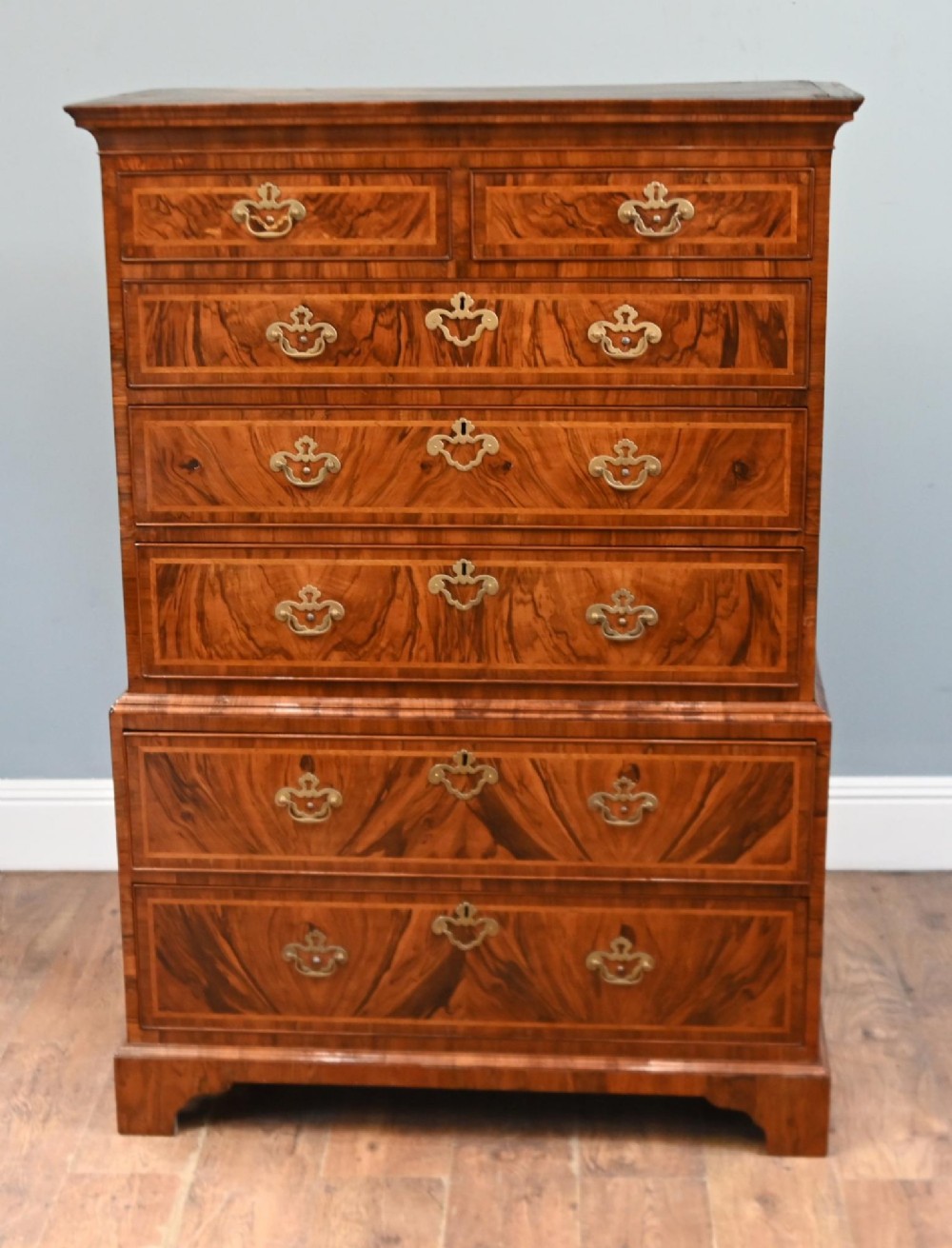 An 18th-century George II walnut chest on chest featuring figured veneered drawer fronts, brass swan-neck handles, and bracket feet.