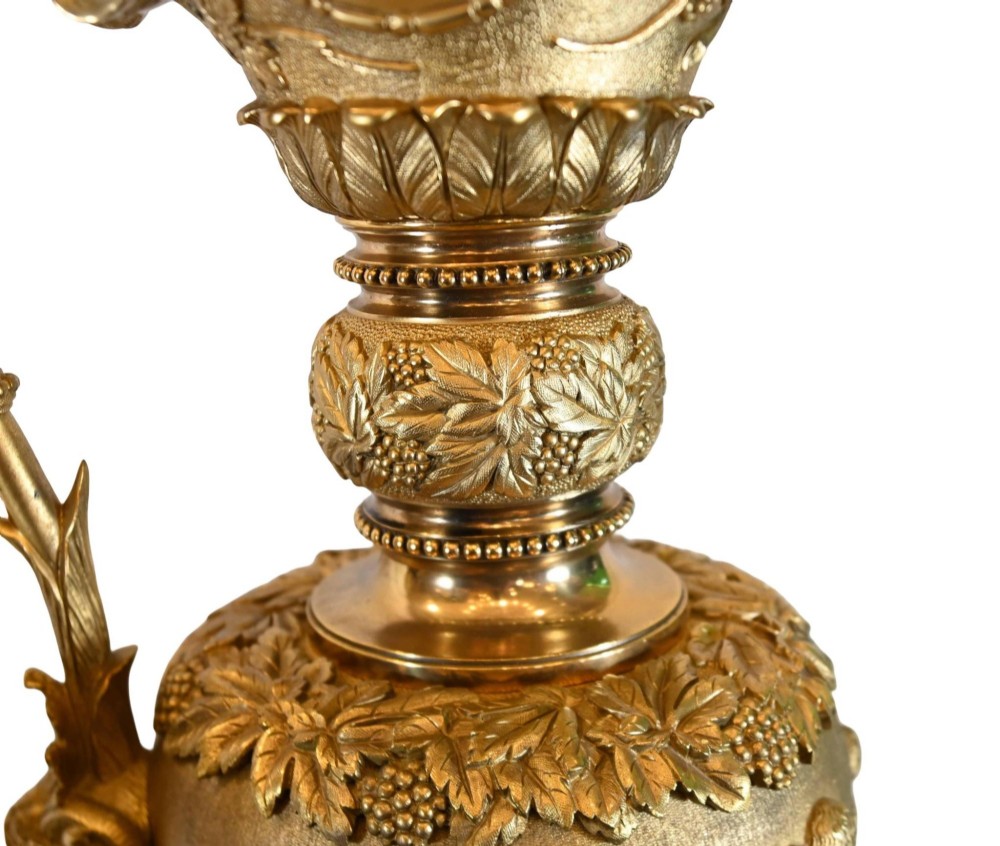 A pair of 19th-century French gilt bronze ewers featuring detailed Bacchus relief scenes, leaf motifs, and cherub-topped handles. View II