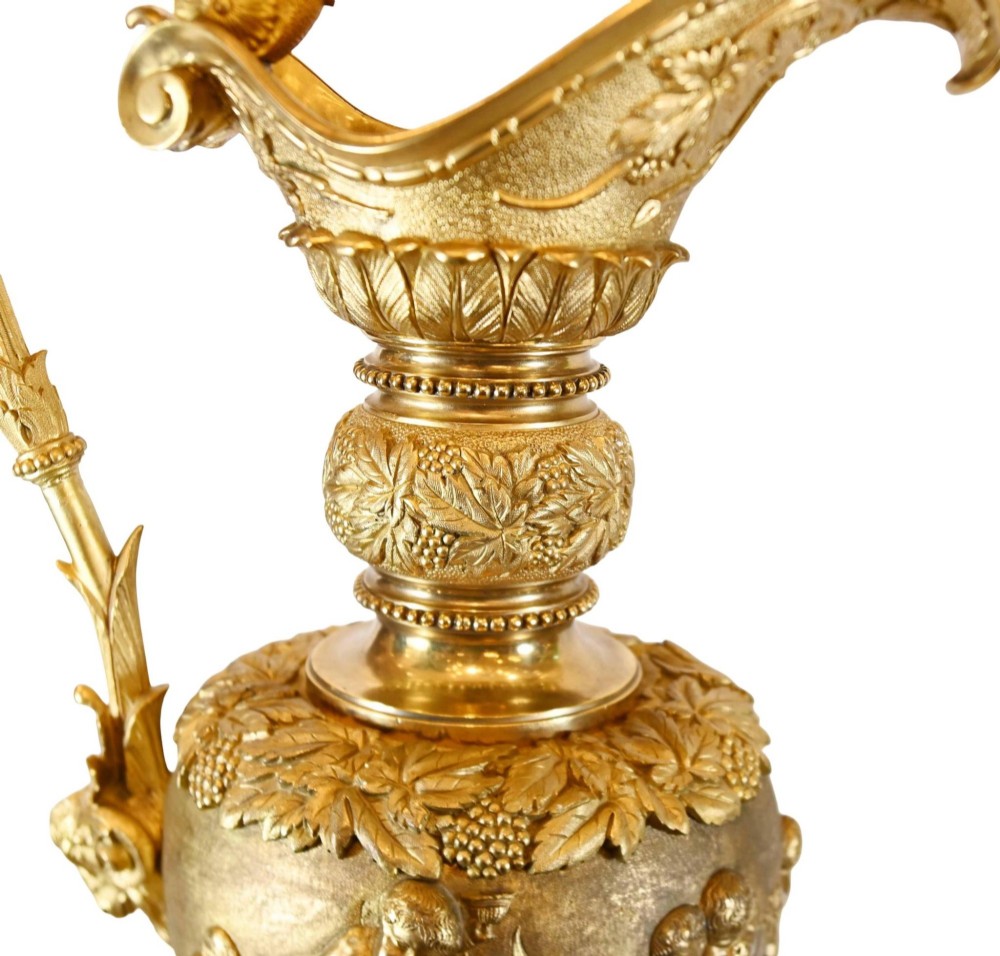 A pair of 19th-century French gilt bronze ewers featuring detailed Bacchus relief scenes, leaf motifs, and cherub-topped handles. View VI
