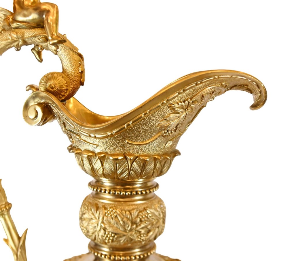 A pair of 19th-century French gilt bronze ewers featuring detailed Bacchus relief scenes, leaf motifs, and cherub-topped handles. View VII