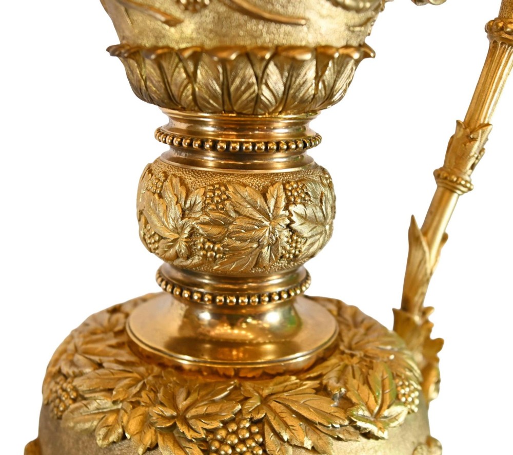 A pair of 19th-century French gilt bronze ewers featuring detailed Bacchus relief scenes, leaf motifs, and cherub-topped handles. View IX