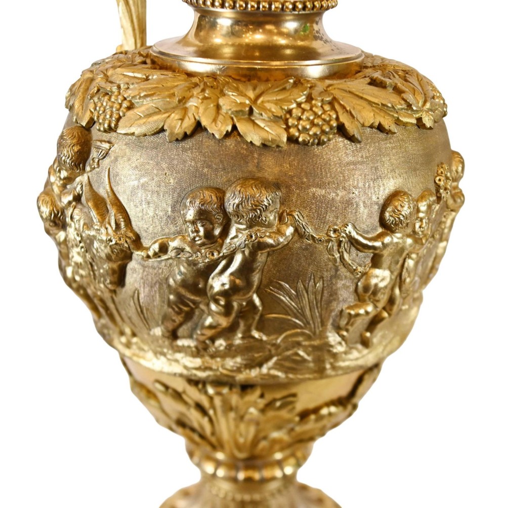 A pair of 19th-century French gilt bronze ewers featuring detailed Bacchus relief scenes, leaf motifs, and cherub-topped handles. View XI