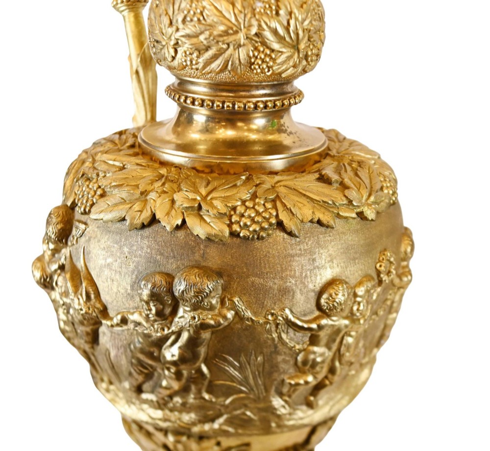 A pair of 19th-century French gilt bronze ewers featuring detailed Bacchus relief scenes, leaf motifs, and cherub-topped handles. View XII