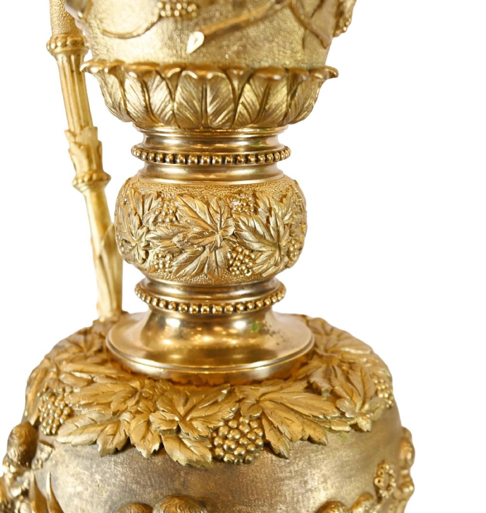 A pair of 19th-century French gilt bronze ewers featuring detailed Bacchus relief scenes, leaf motifs, and cherub-topped handles. View XIII