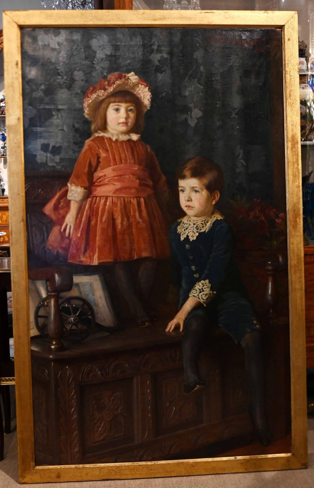 An 1887 Victorian oil portrait painting depicting two young children in period attire seated on a carved wooden bench within a gilt wood frame.