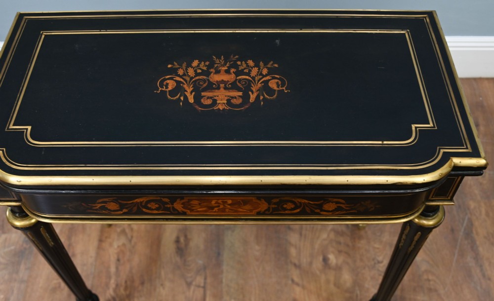 A late 19th-century French Napoleon III ebonised card table featuring floral marquetry inlay on the top and frieze with brass borders and tapered fluted legs. View II