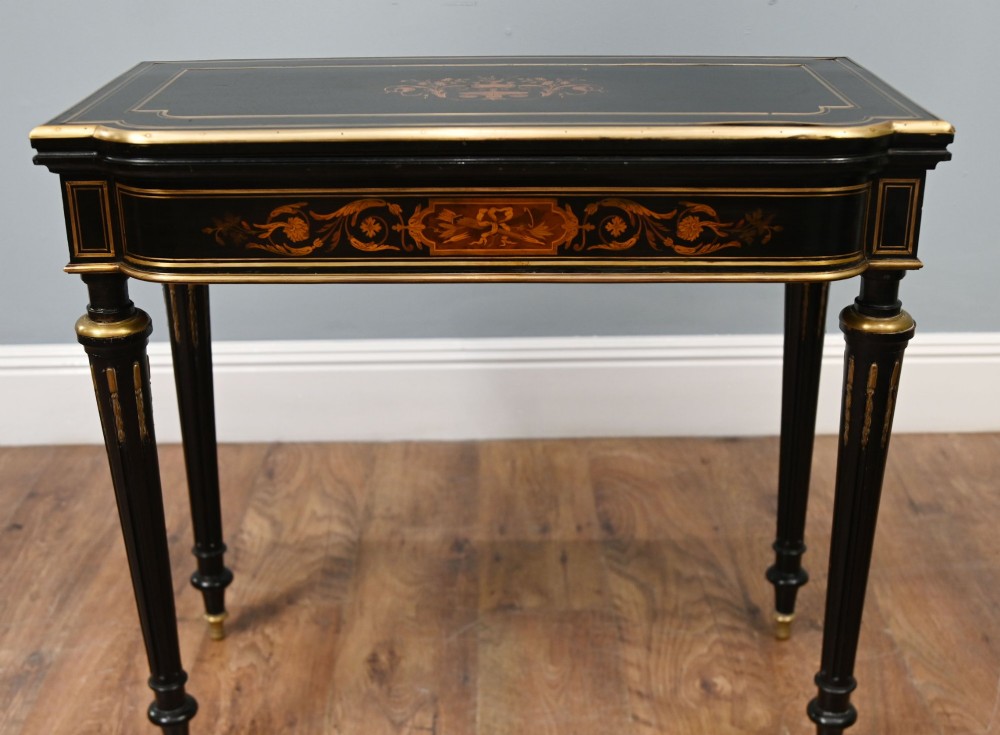 A late 19th-century French Napoleon III ebonised card table featuring floral marquetry inlay on the top and frieze with brass borders and tapered fluted legs. View IV