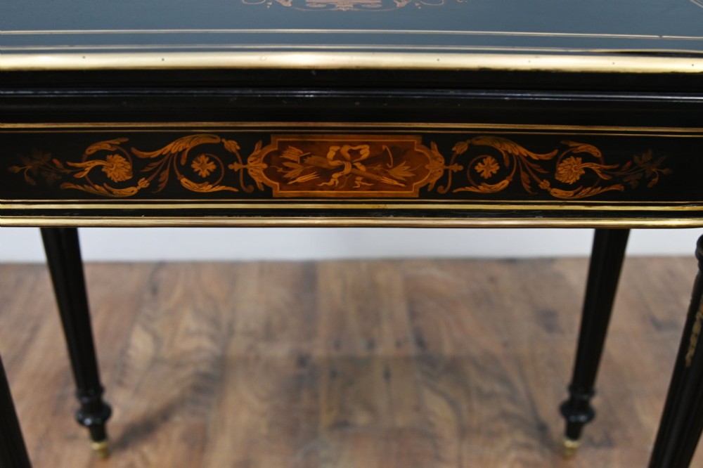A late 19th-century French Napoleon III ebonised card table featuring floral marquetry inlay on the top and frieze with brass borders and tapered fluted legs. View V