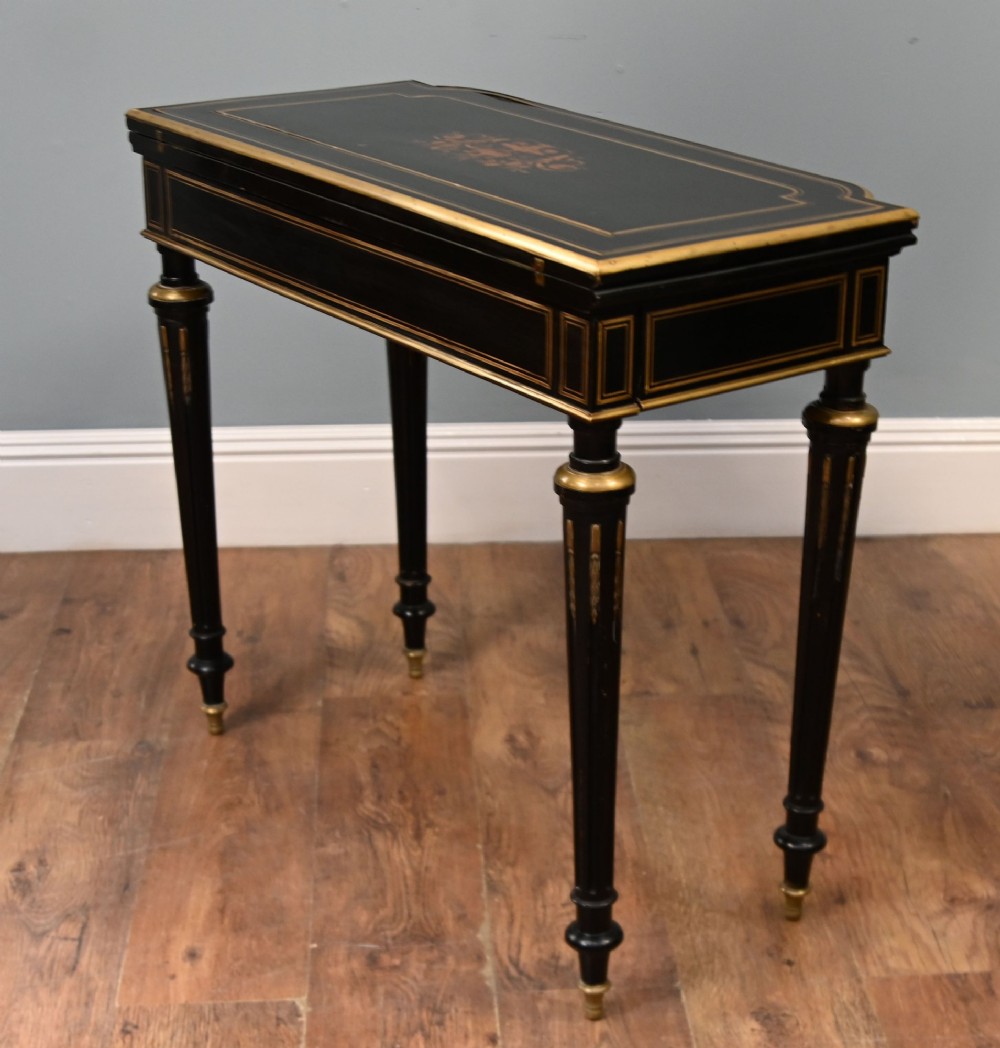 A late 19th-century French Napoleon III ebonised card table featuring floral marquetry inlay on the top and frieze with brass borders and tapered fluted legs. View VIII