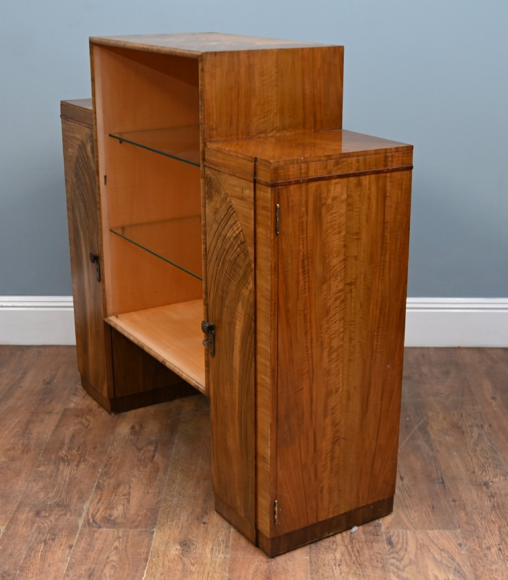 An Art Deco figured walnut display cabinet with a raised central open section containing two glass shelves, flanked by two side cupboards with arched veneer detailing. View IV